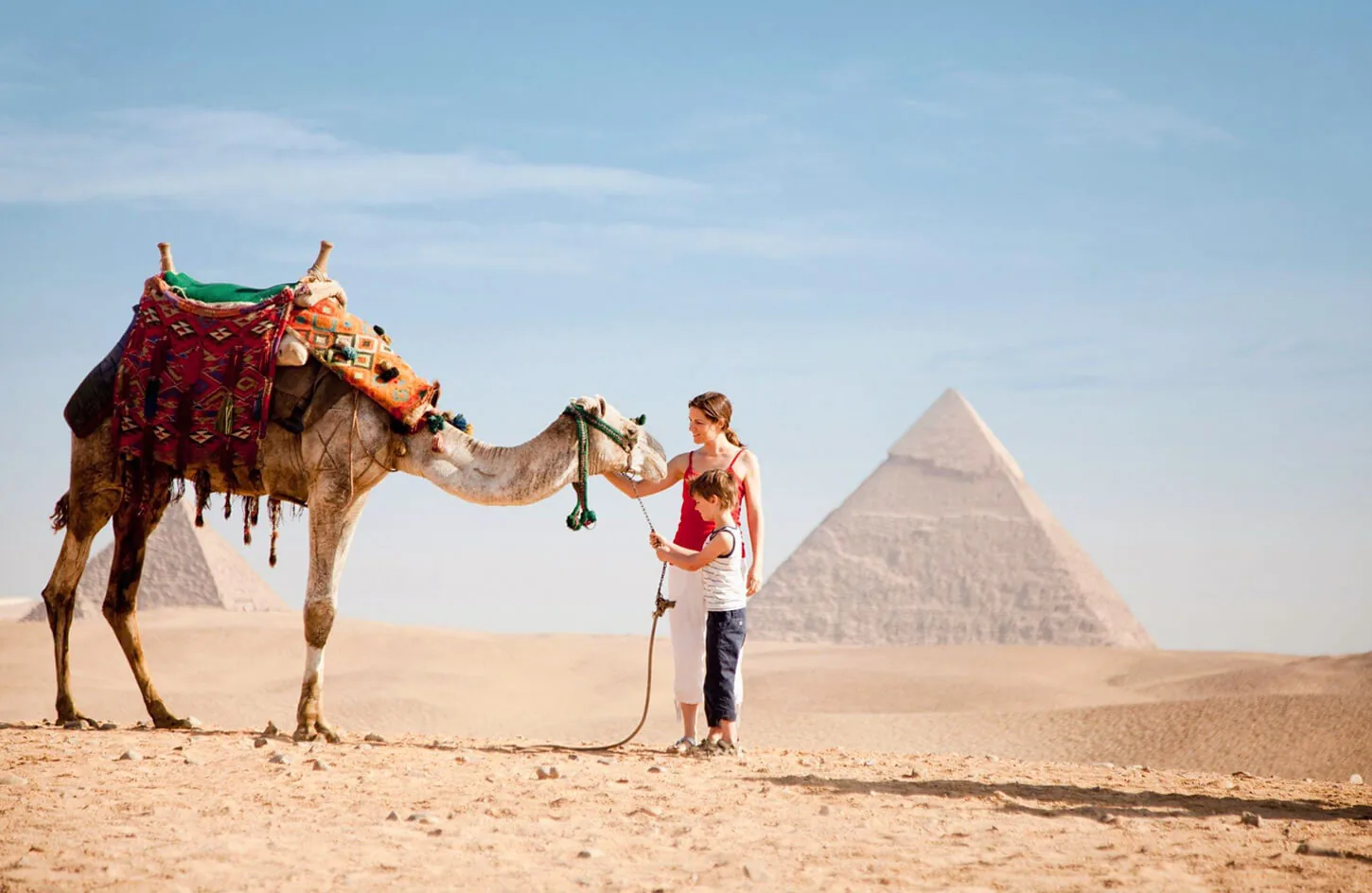 A little boy and his mother with a camel in front of the pyramids