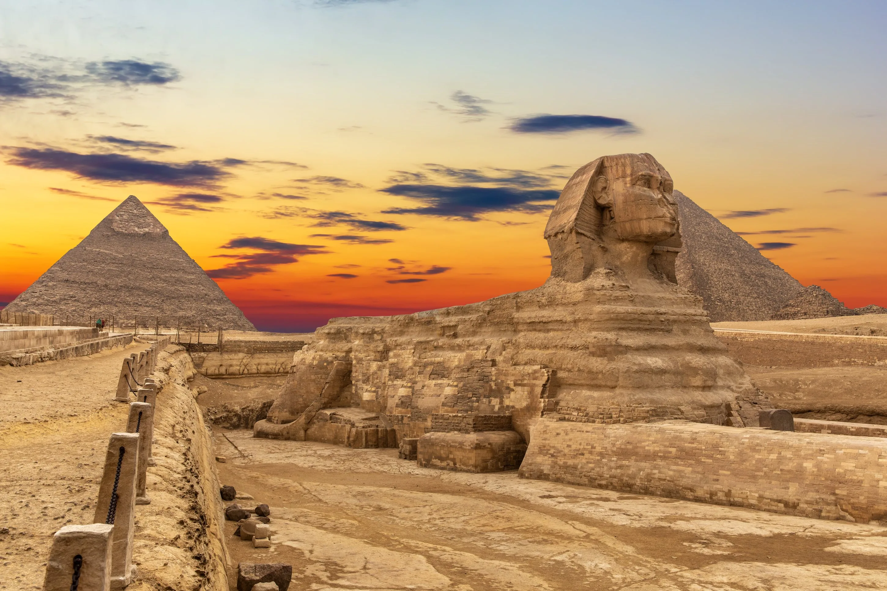 Great Sphinx and Giza Pyramids against an orange sunset sky